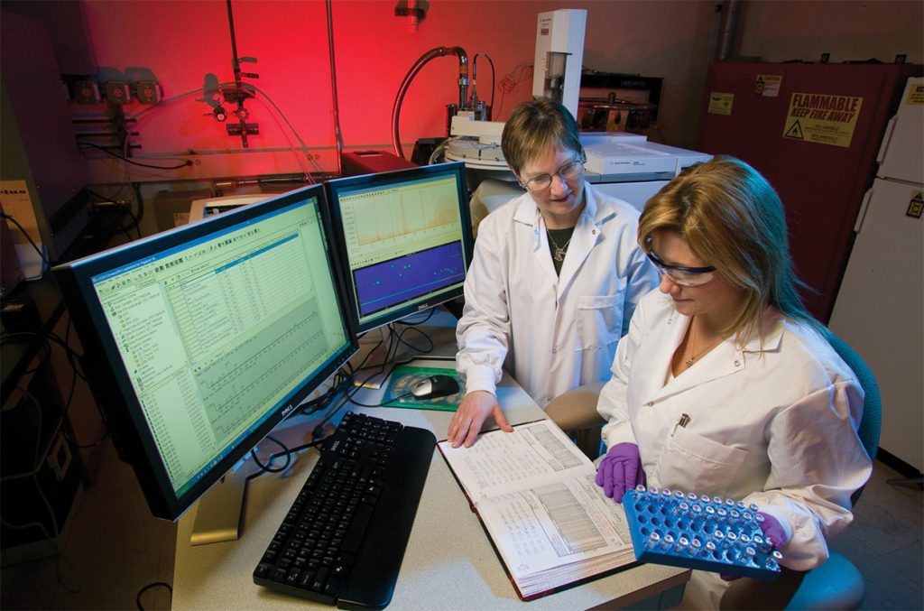 Women working in a lab with white lab coats on in front of books and computers