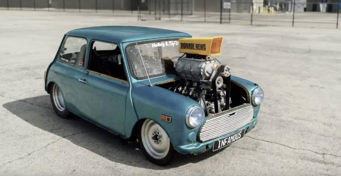 a large F1 engine in a classic, old, beat up blue mini coop